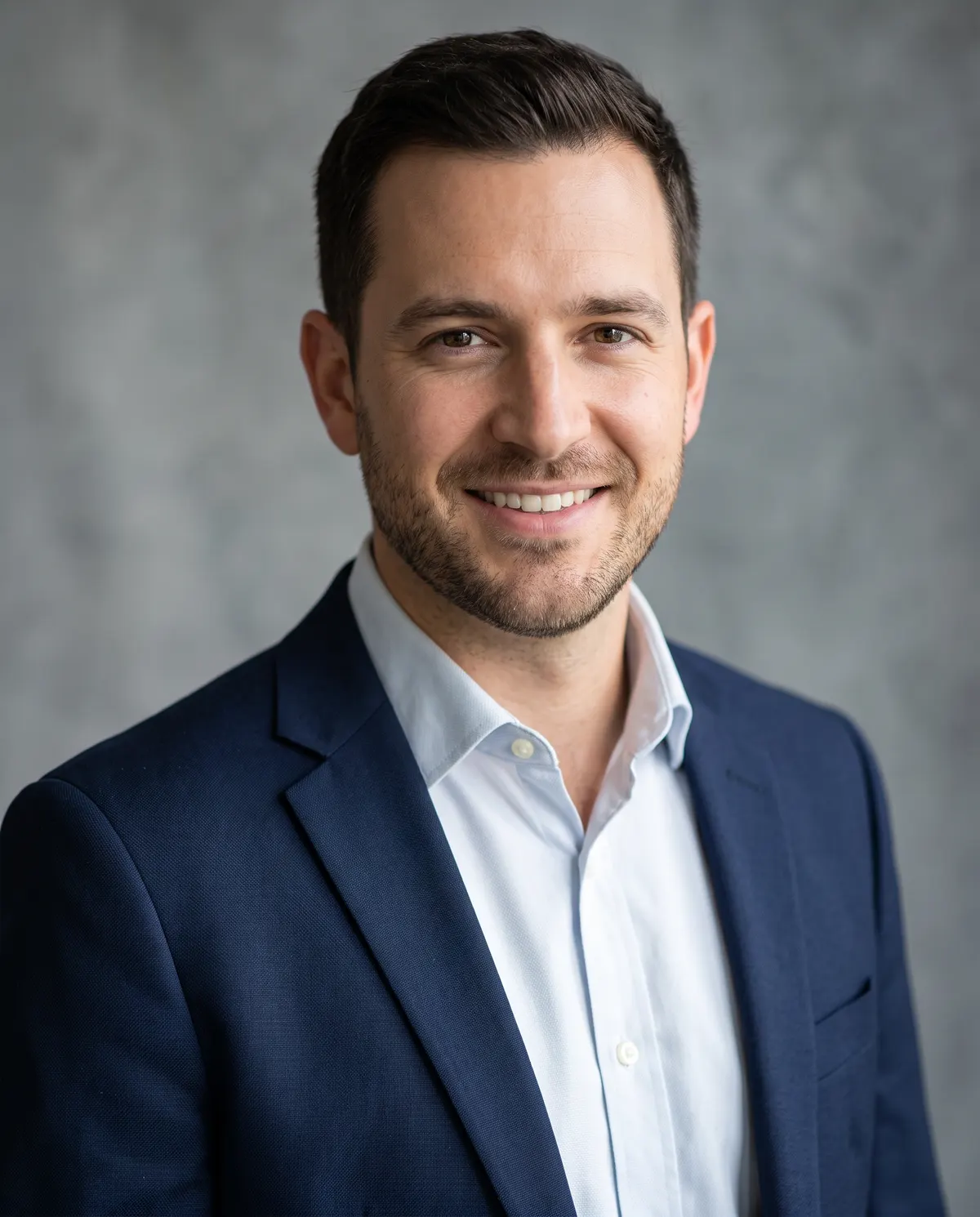 Professional studio headshot of a smiling man in a navy blazer